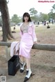 A woman in a pink skirt and jacket leaning against a fence.