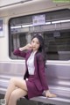 A woman in a purple suit sitting on a subway train.